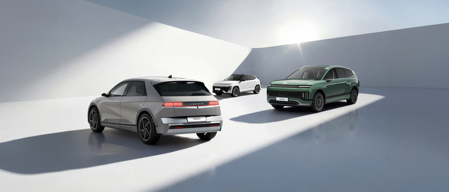 Tre moderne elbiler er parkeret i et rummeligt, hvidt, minimalistisk område oplyst af stærkt sollys.