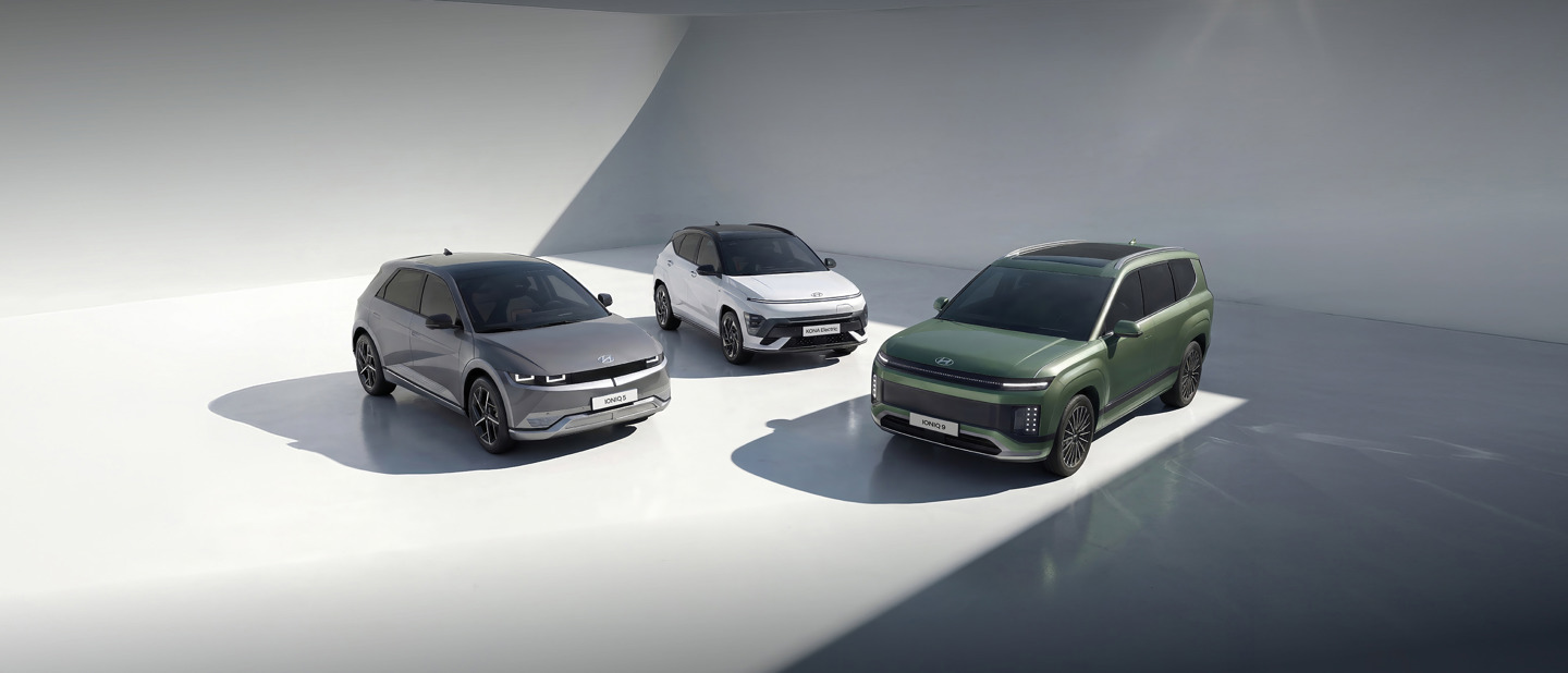 Tre moderne elektriske SUV'er i grå, hvid og grøn er parkeret i et minimalt, solbeskinnet, hvidt indendørs rum.