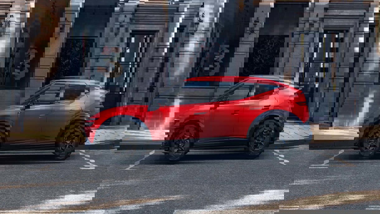 En rød IONIQ 3 parkeret på en gade i byen foran en indgang med glasdøre og lodrette metalstænger.