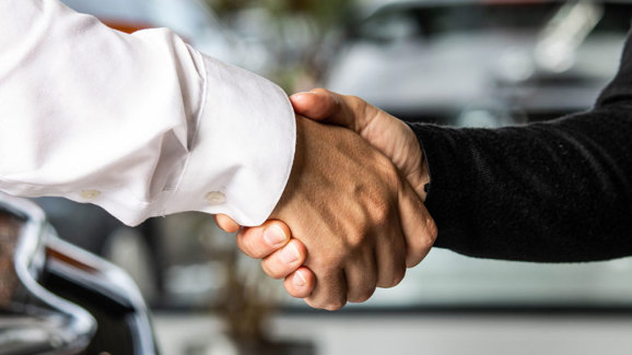 To personer giver hånd, den ene i hvid skjorte og den anden i sort, med sløret baggrund.