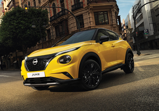 Gul Nissan Juke Hybrid i gademiljø med træer