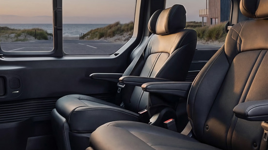To sorte lædersæder inde i en bil med et kystlandskab, der ses gennem vinduet i baggrunden.