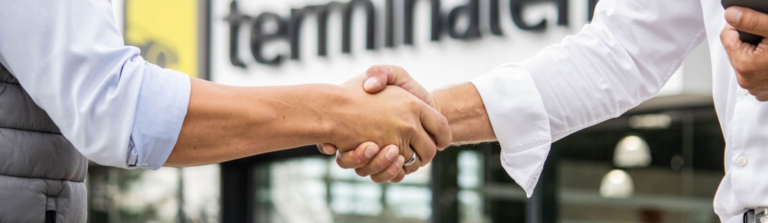 To mennesker giver hinanden hånden foran en bygning med ordet terminal i baggrunden.