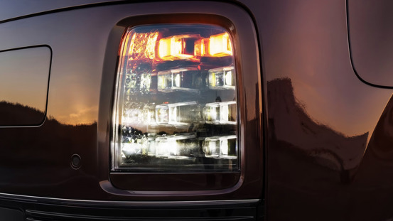 Nærbillede af en STARIE Electric lygte med oplyste LED-elementer, der reflekterer solnedgangen og det omgivende landskab.