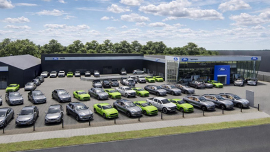 En bilforhandlerplads med mange biler, nogle i lysegrønt, parkeret uden for Ford-mærkede bygninger på en solrig dag.